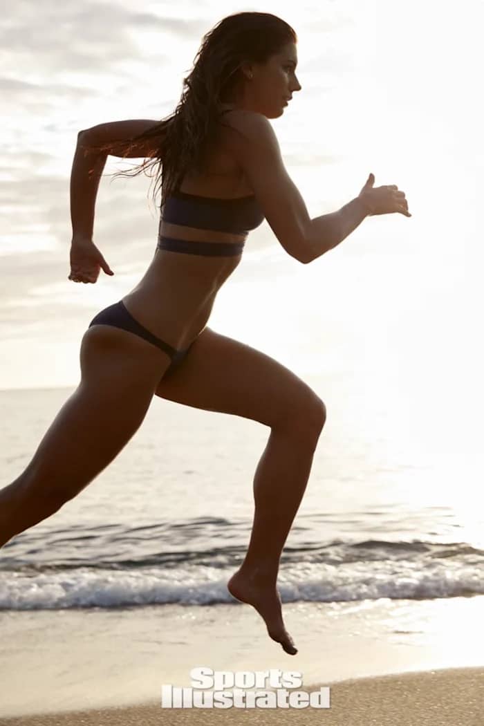 Alex Morgan runs on the sand at sunset in a dark bikini set.